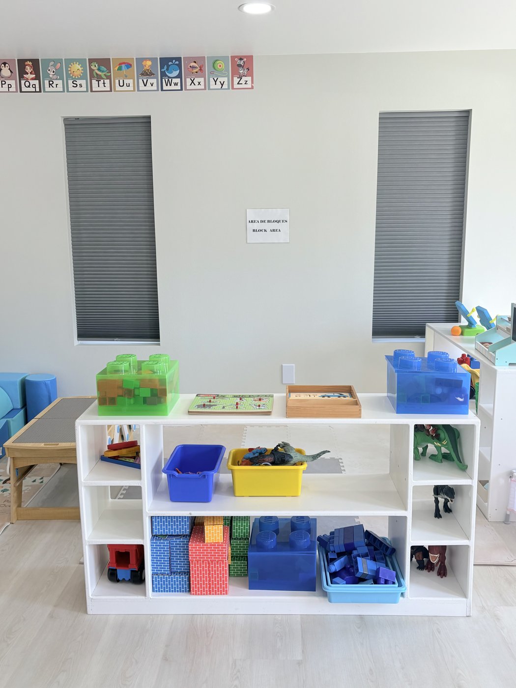 Block area shelf stocked with building blocks, dinosaurs and a Lego table under alphabet cards