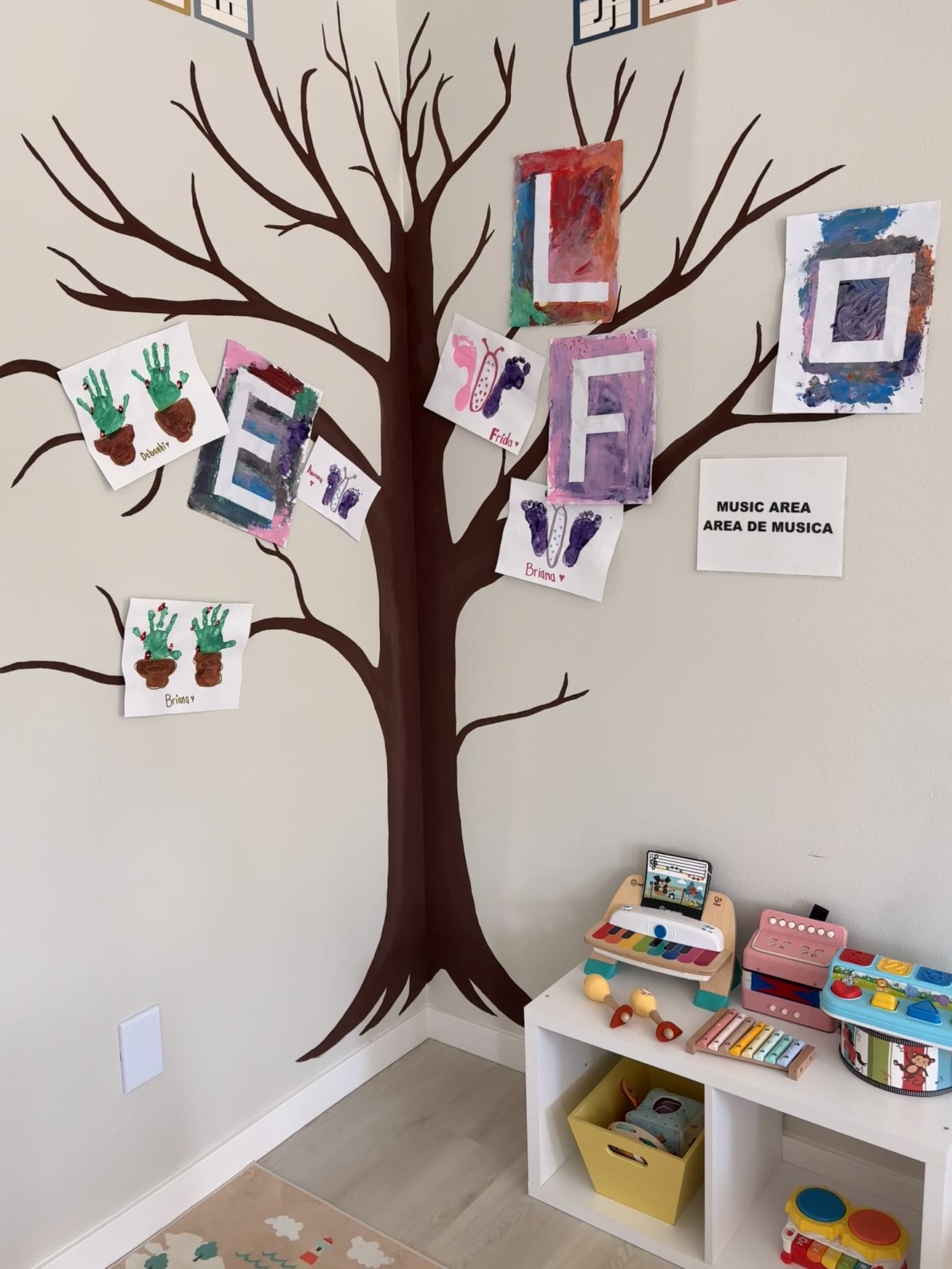 Classroom tree mural displaying children's painted artwork above the music area shelf