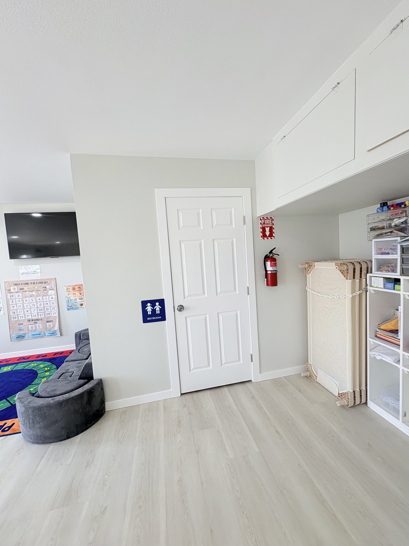 Quiet hallway area with folded nap cots, restroom access and a soft seating corner